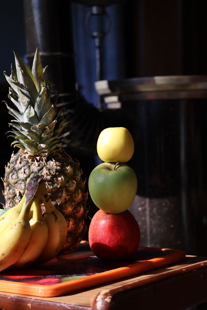 Una vibrante pila de frutas que incluye manzanas, plátanos y piña bajo una iluminación cálida.