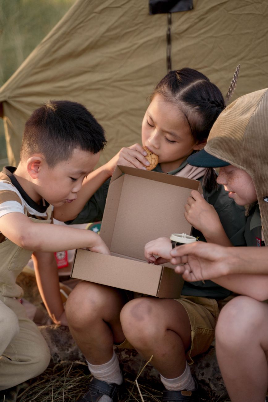 Tres niños compartiendo aperitivos al aire libre en un campamento de verano.