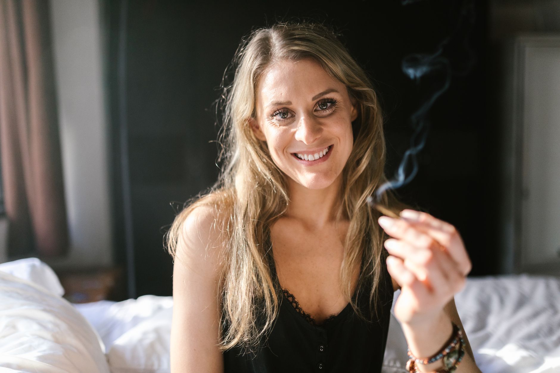 Mujer sonriente sosteniendo un porro en un ambiente relajado de interior, celebrando la cultura cannábica.